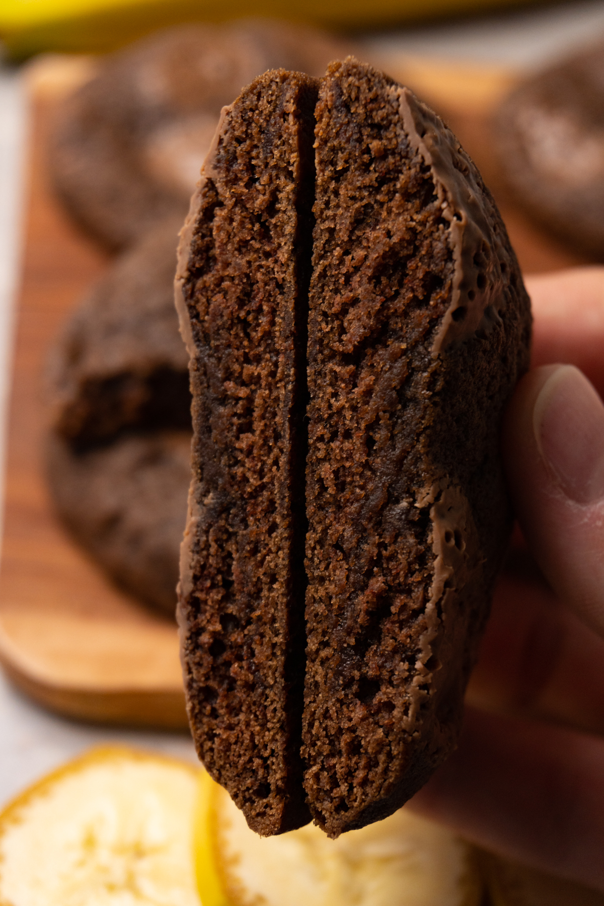 A hand is holding a chocolate cookie with chocolate chips that has been cut in half.