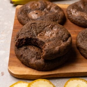 A stack of cookies on a wooden board; a bite has been taken from the top cookie.