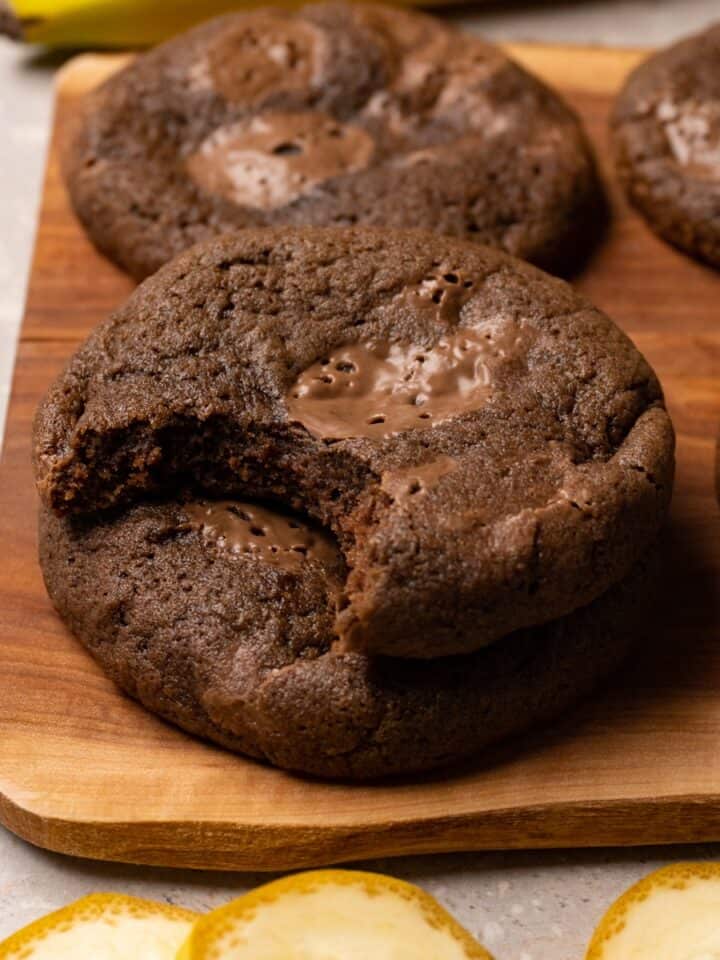 A stack of cookies on a wooden board; a bite has been taken from the top cookie.