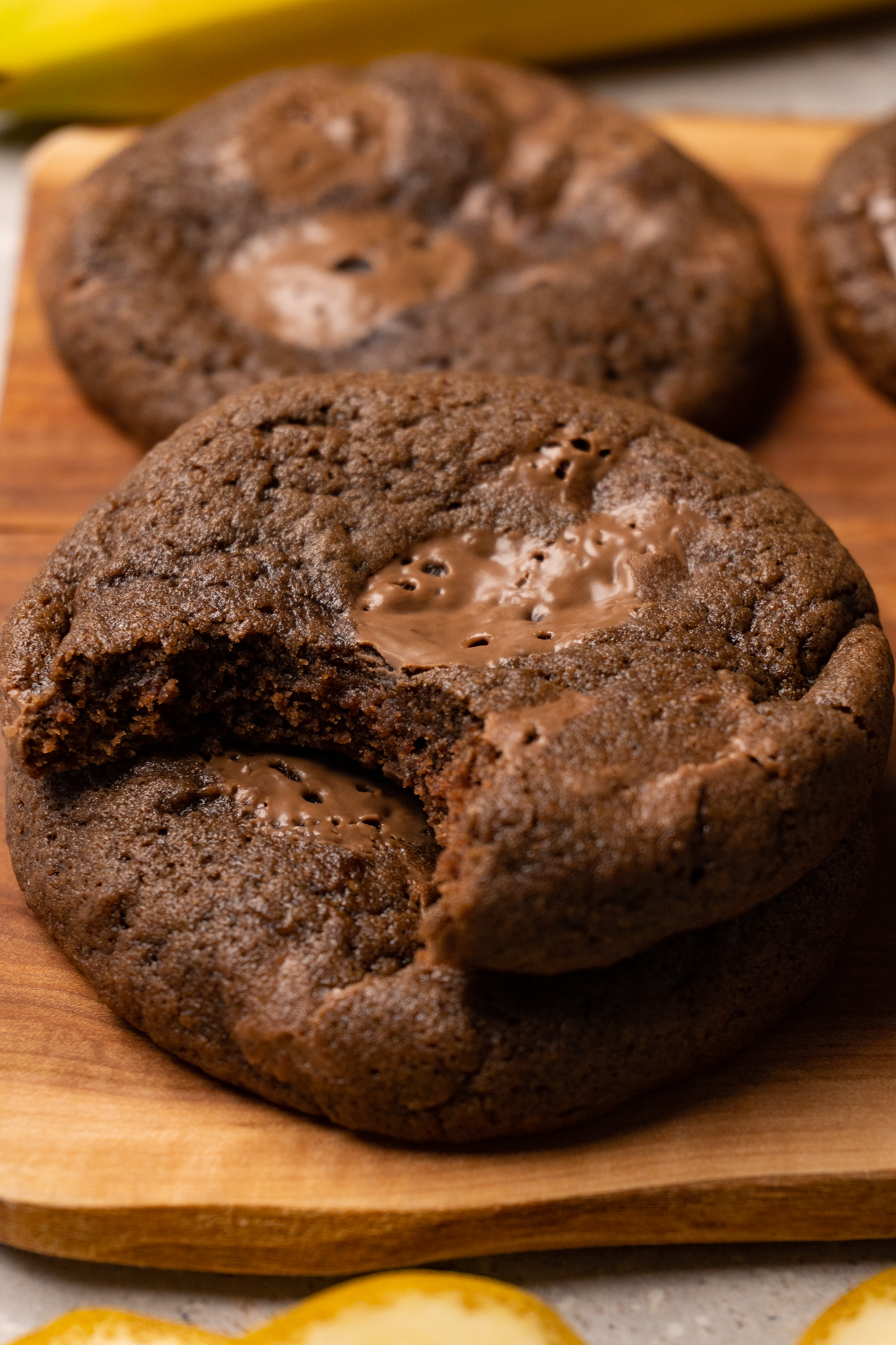 A stack of cookies on a wooden board; a bite has been taken from the top cookie.