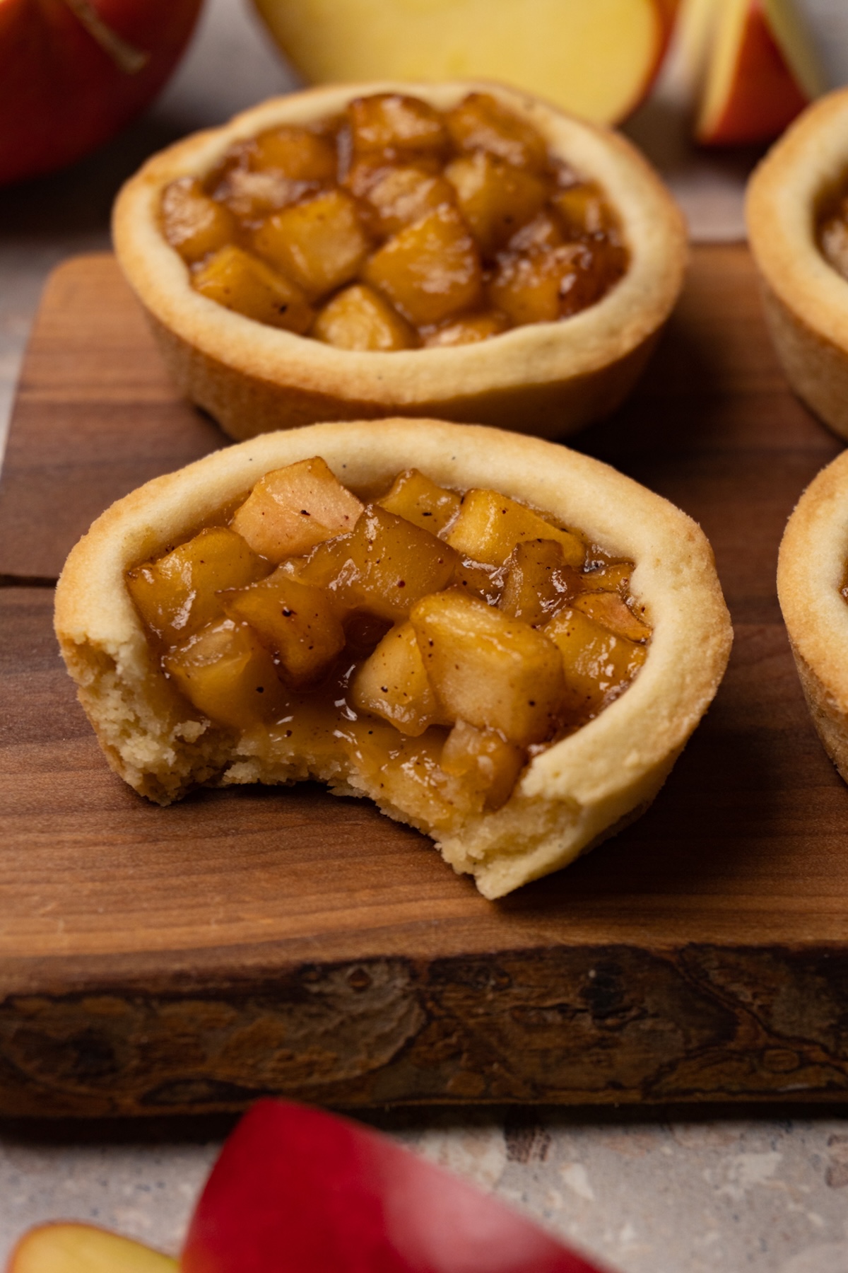 Cookies with an apple filling are served on a wooden board. One of them has a bite taken out of it.