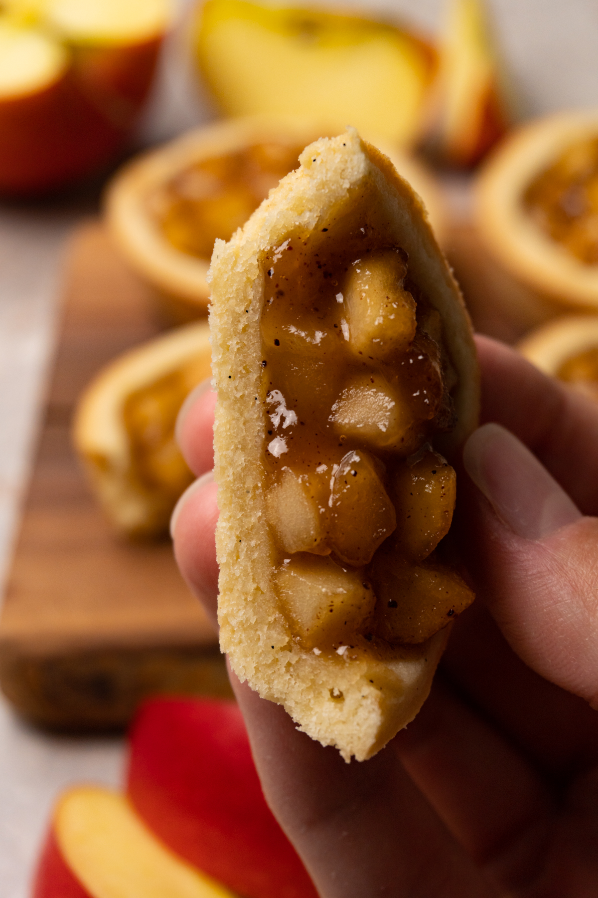 A hand holds a halved cookie with apple filling.