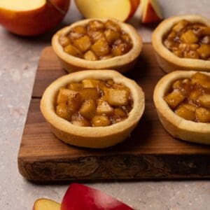 Cookies with an apple filling are served on a wooden board.