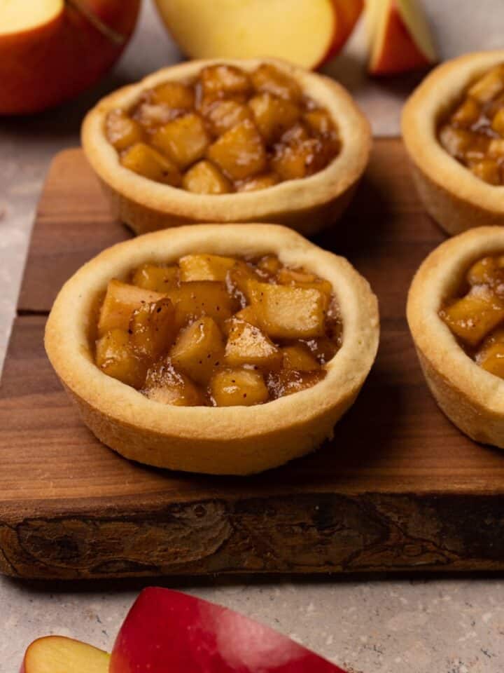 Cookies with an apple filling are served on a wooden board.